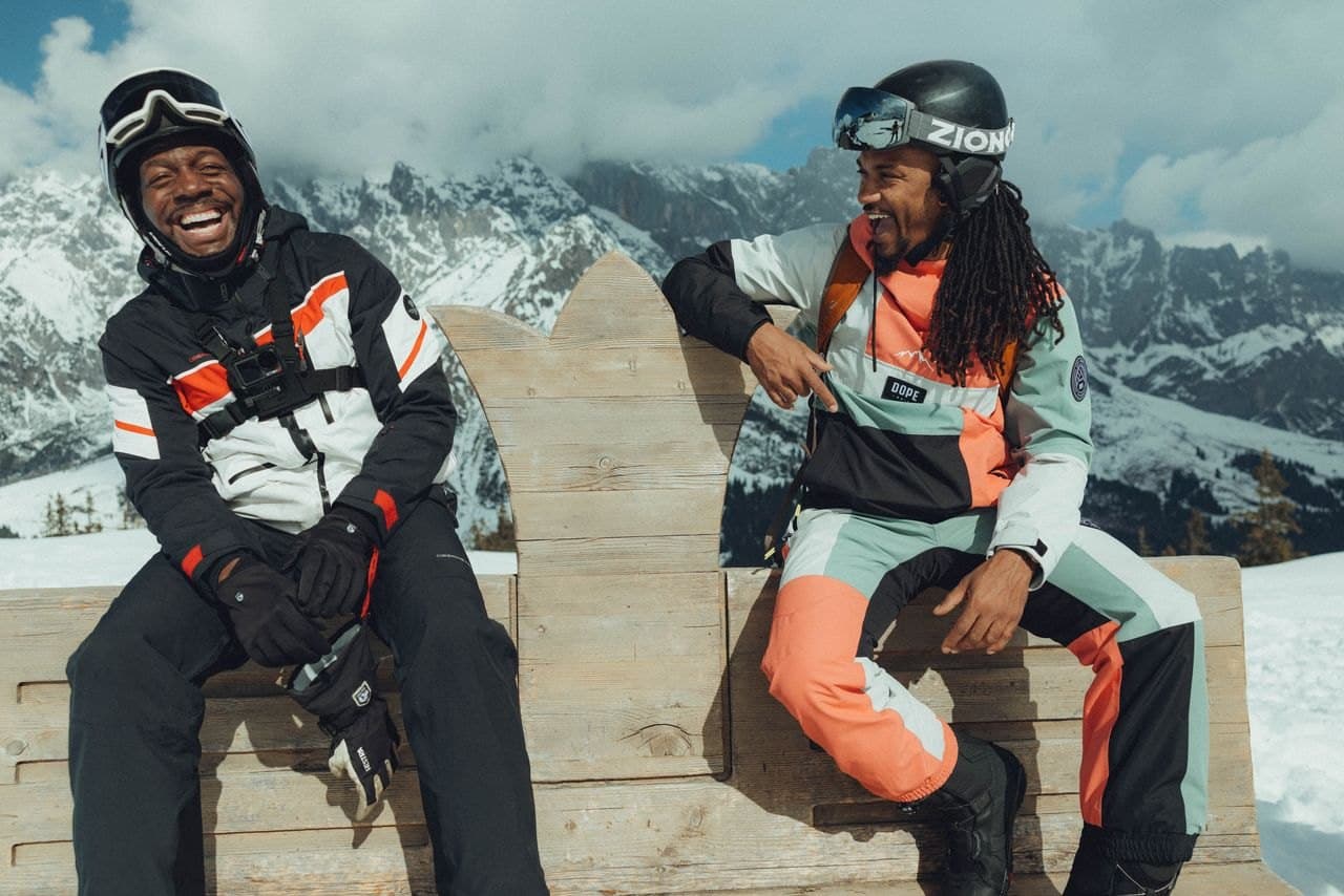 Two riders laughing on a wooden bench above the mountains