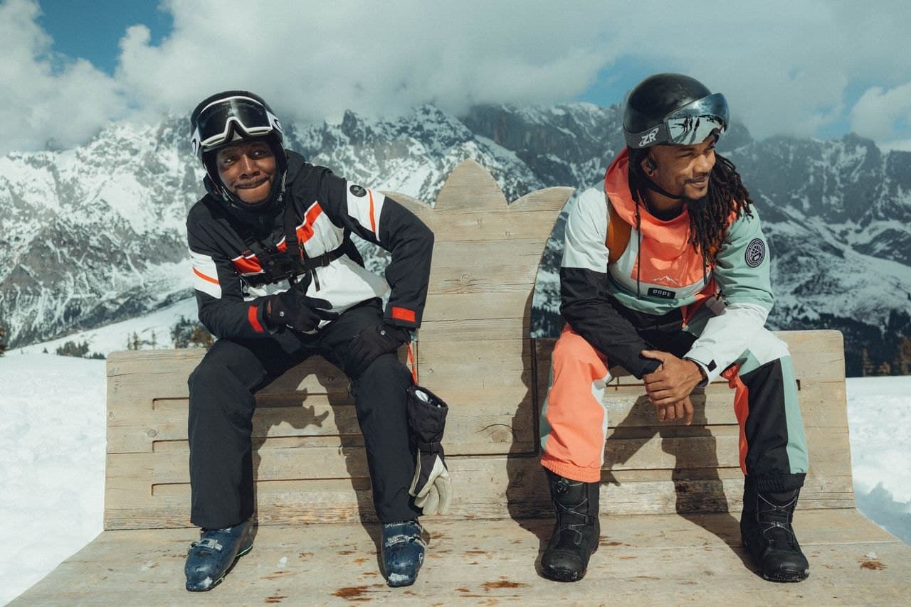 Two riders sitting on a wooden bench with peaks behind them